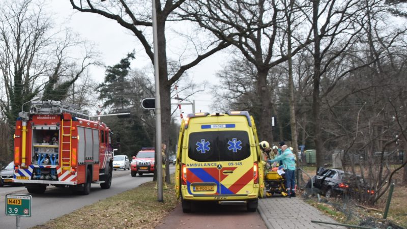 Auto dwars door hek tegen boom naast de weg